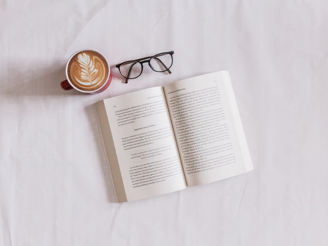 An open book, eyeglasses, and a cup of coffee.