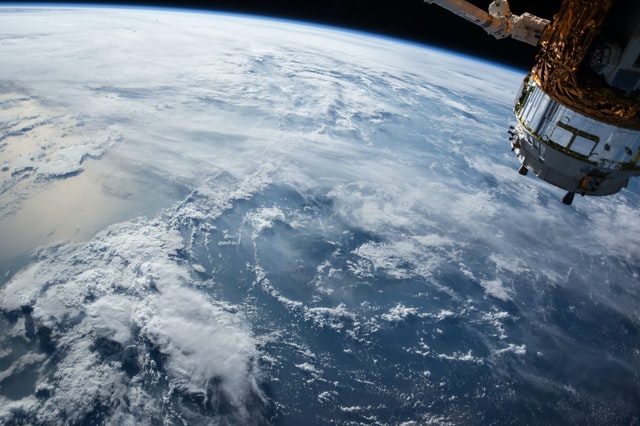 Clouds over the ocean seen from space. An artificial satellite is visible over the planet.